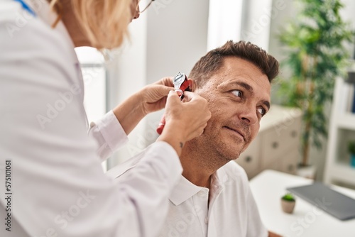 Middle age man and woman doctor and patient examining ear having medical consultation at clinic