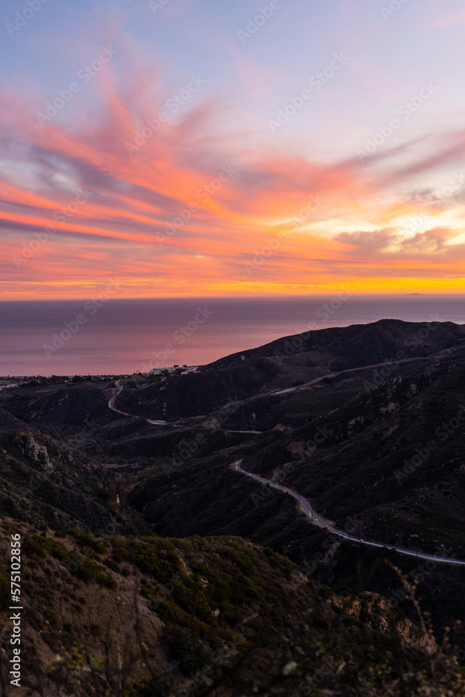 Sun setting horizon and mountains. Photo taken from a lookout in the Santa Monica mountains in Malibu. Headlights and taillights of cars in traffic are seen on the meandering and scenic PCH