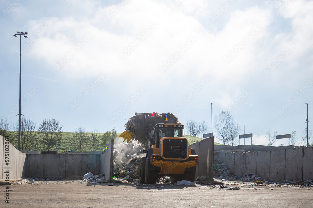 Yellow wheel loader, with lifted scrap grapple, moving along the recycling center area in process handling dumped waste