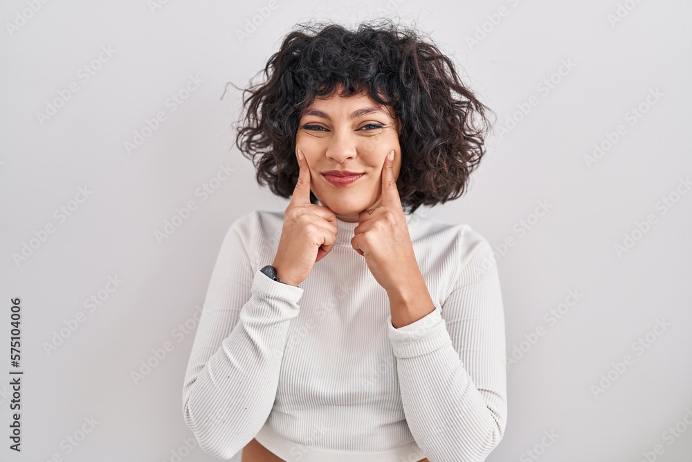Hispanic woman with curly hair standing over isolated background smiling with open mouth, fingers pointing and forcing cheerful smile Hispanic woman with curly hair standing over isolated background smiling with open mouth, fingers pointing and forcing cheerful smile