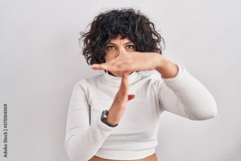 Hispanic woman with curly hair standing over isolated background doing time out gesture with hands, frustrated and serious face Hispanic woman with curly hair standing over isolated background doing time out gesture with hands, frustrated and serious face