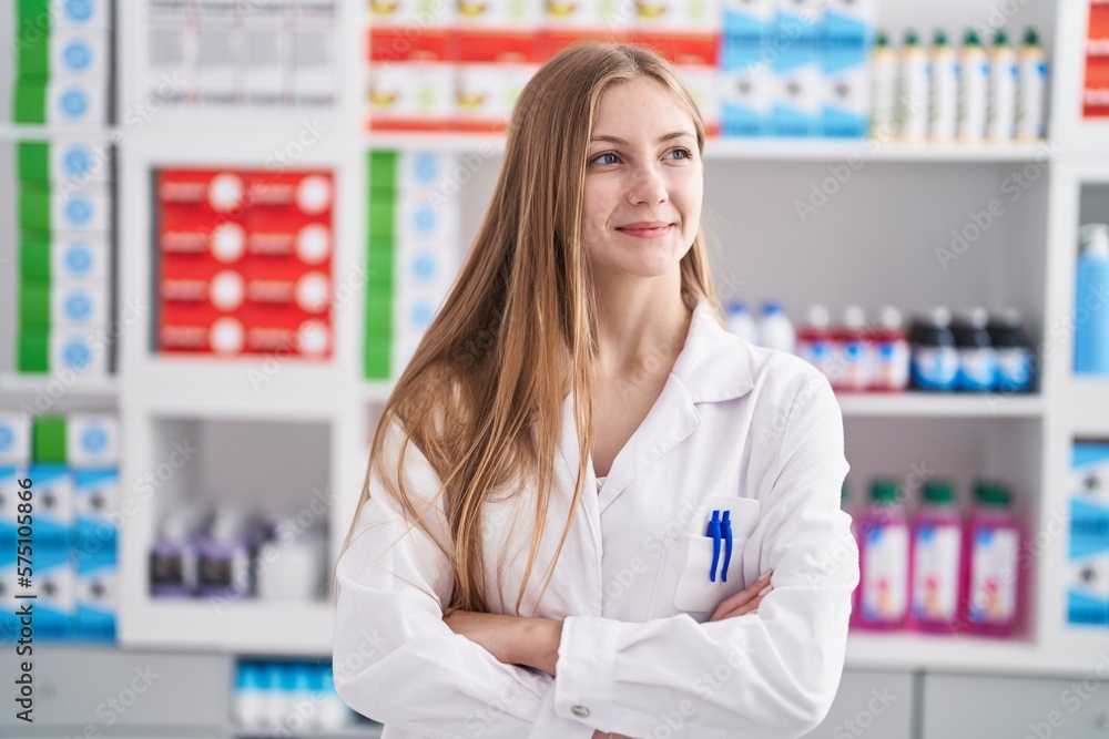 Young caucasian woman pharmacist smiling confident standing with arms crossed gesture at pharmacy