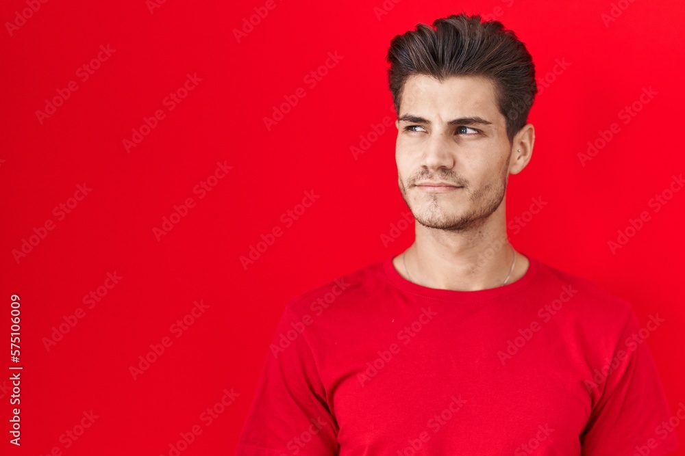 Young hispanic man standing over red background smiling looking to the side and staring away thinking. Young hispanic man standing over red background smiling looking to the side and staring away thinking.