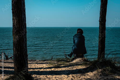 A lonely woman sitting between trees and watching to a calm and silent see meditating