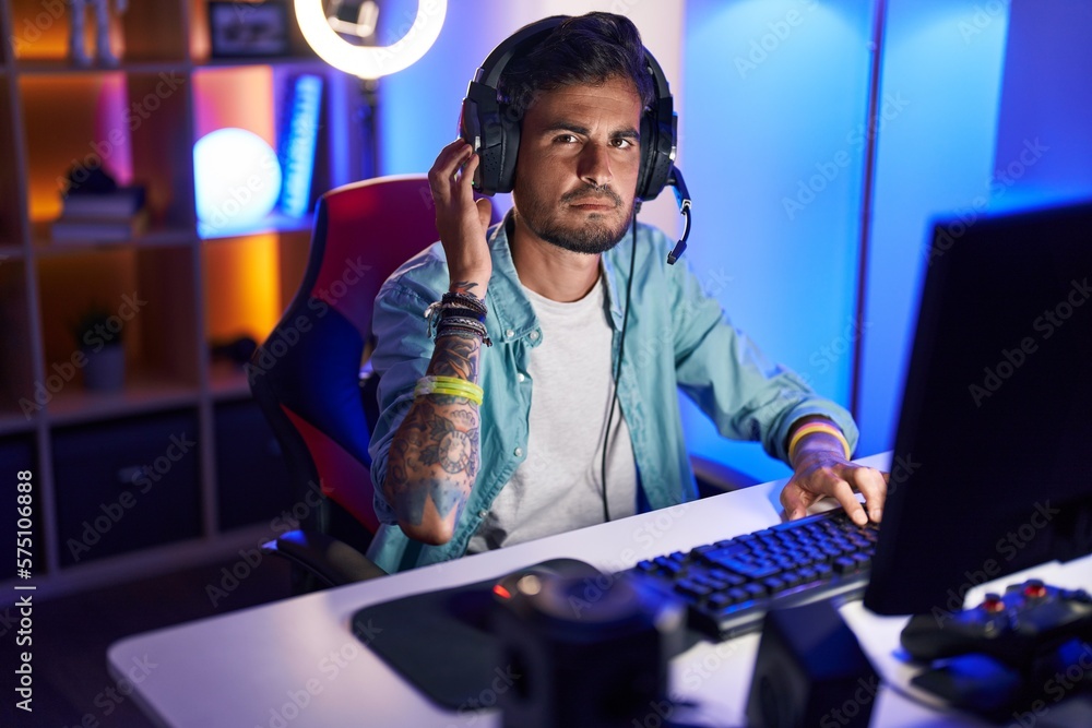 Young hispanic man streamer sitting on table with relaxed expression at gaming room Young hispanic man streamer sitting on table with relaxed expression at gaming room