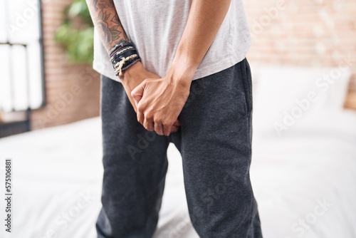 Young hispanic man covering his genitals with hands at bedroom