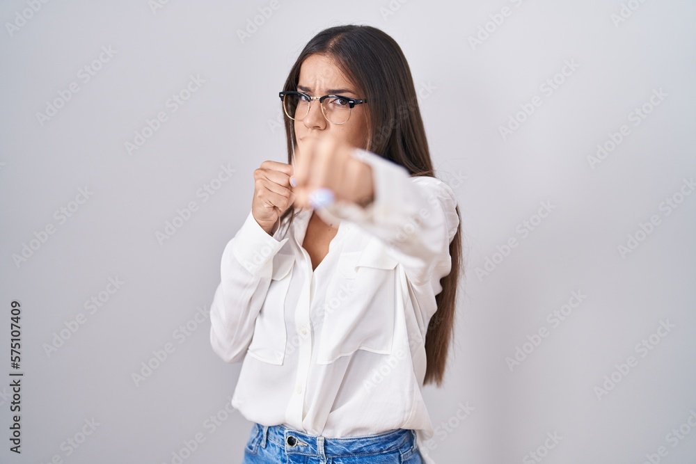 Young brunette woman wearing glasses ready to fight with fist defense gesture, angry and upset face, afraid of problem Young brunette woman wearing glasses ready to fight with fist defense gesture, angry and upset face, afraid of problem