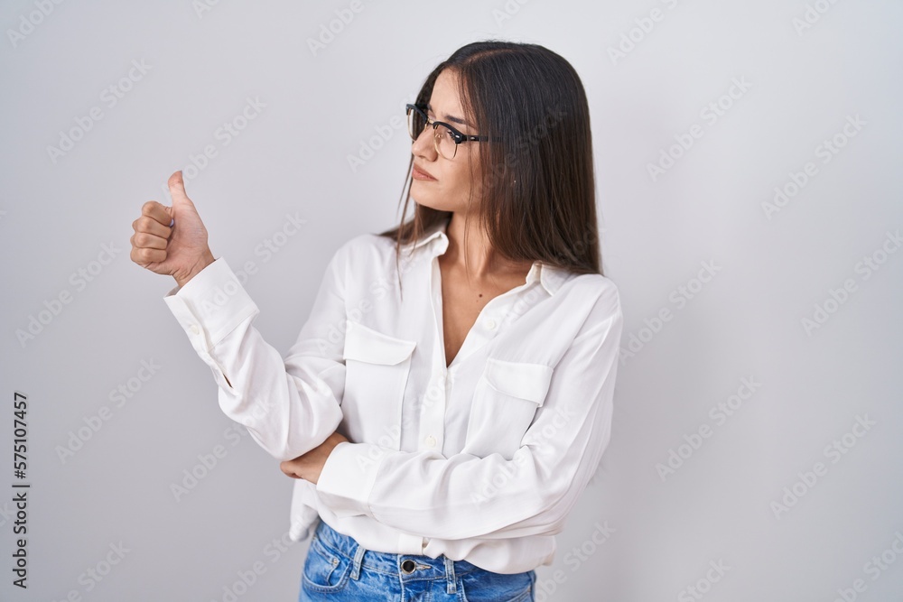 Young brunette woman wearing glasses looking proud, smiling doing thumbs up gesture to the side Young brunette woman wearing glasses looking proud, smiling doing thumbs up gesture to the side
