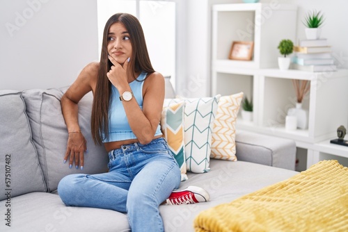 Young brunette woman sitting on the sofa at home thinking worried about a question, concerned and nervous with hand on chin
