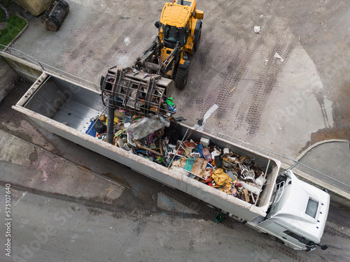 Skid steer loader loading a truck with waste material transferred for further sorting, treatment, and recycling, aerial view. Waste management