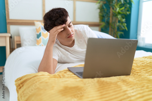 Non binary man using laptop with worried expression at bedroom