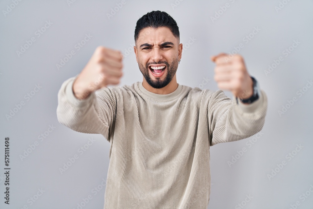 Young handsome man standing over isolated background angry and mad raising fists frustrated and furious while shouting with anger. rage and aggressive concept. Young handsome man standing over isolated background angry and mad raising fists frustrated and furious while shouting with anger. rage and aggressive concept.