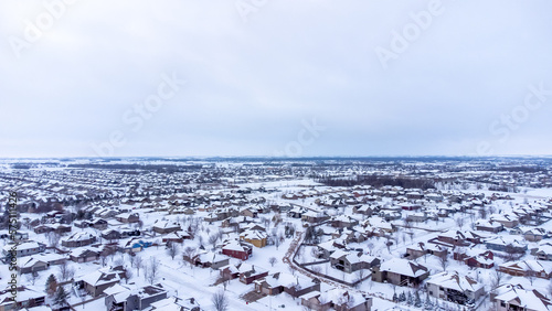 Aerial drone view of a snow covered suburban residential neighborhood with rows of white roofs and houses. 