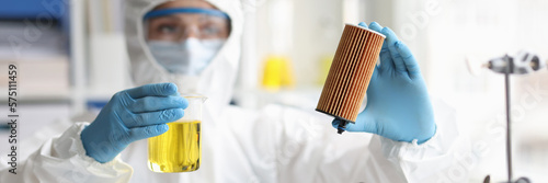 Scientist in protective suit holds car filter cartridge in laboratory and oil