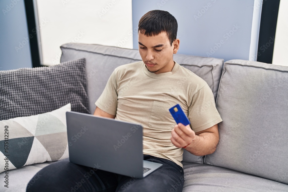 Young man using laptop and credit card sitting on sofa at home Young man using laptop and credit card sitting on sofa at home