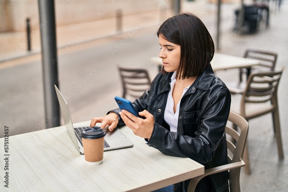Fototapeta premium Young beautiful hispanic woman using smartphone sitting on table at coffee shop terrace