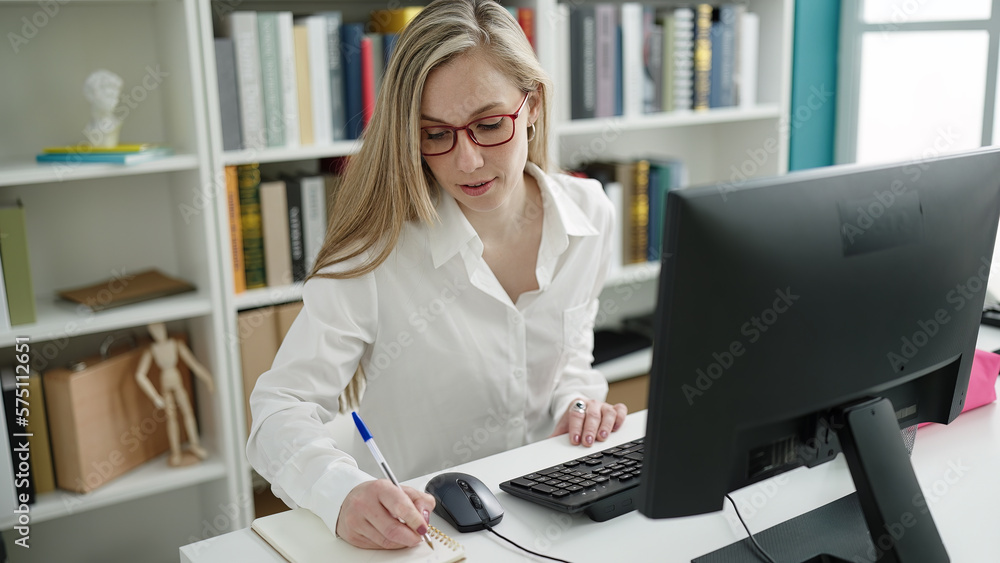 Young blonde woman student using computer writing on notebook at library university Young blonde woman student using computer writing on notebook at library university