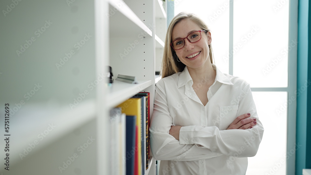 Young blonde woman teacher standing with relaxed expression and arms ...
