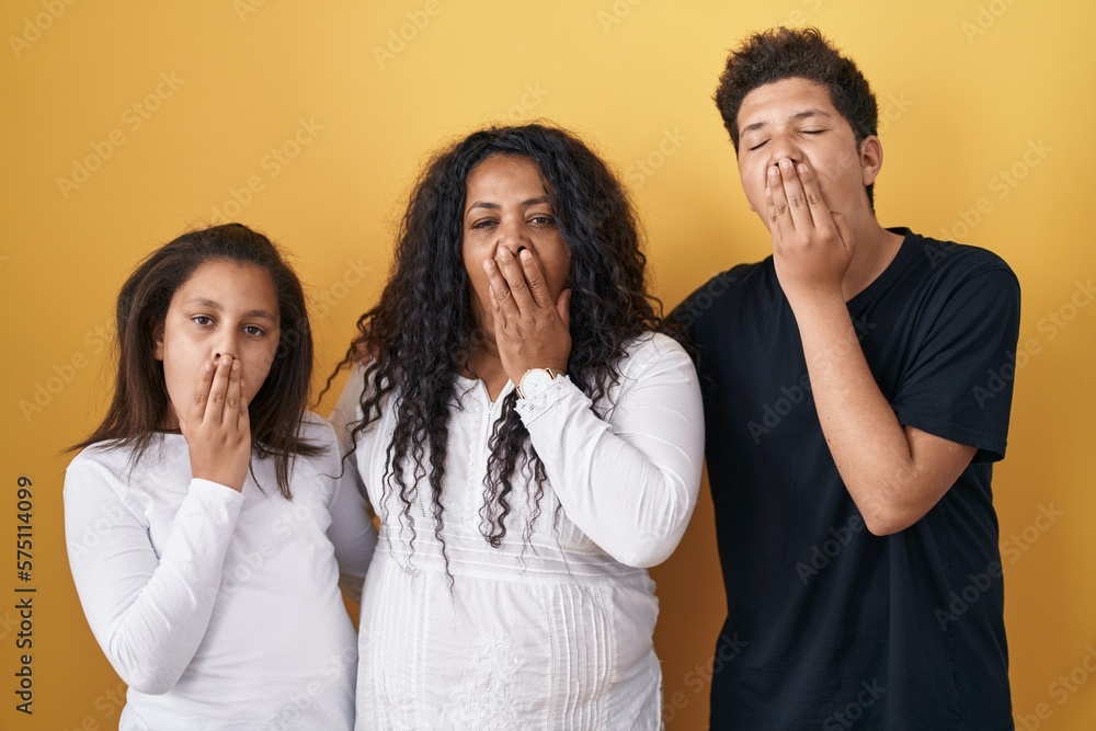 Family of mother, daughter and son standing over yellow background bored yawning tired covering mouth with hand. restless and sleepiness. Family of mother, daughter and son standing over yellow background bored yawning tired covering mouth with hand. restless and sleepiness.