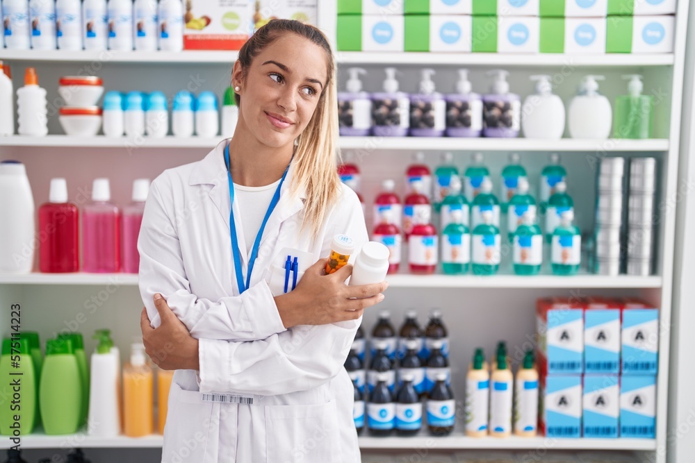 Young beautiful hispanic woman pharmacist holding pills bottles with arms crossed gesture at pharmacy