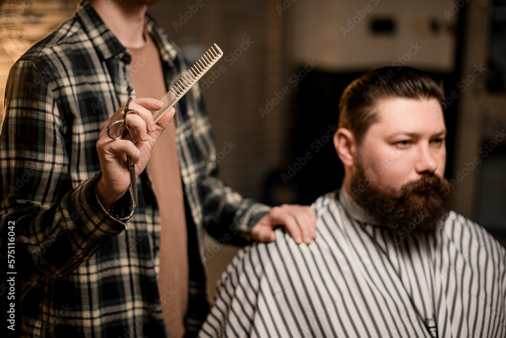 view on bearded man client and male barber with comb in his hand view on bearded man client and male barber with comb in his hand