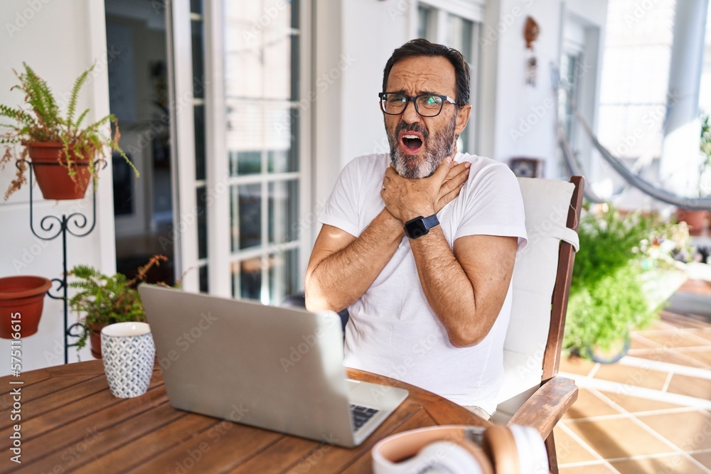 Fototapeta premium Middle age man using computer laptop at home shouting suffocate because painful strangle. health problem. asphyxiate and suicide concept.