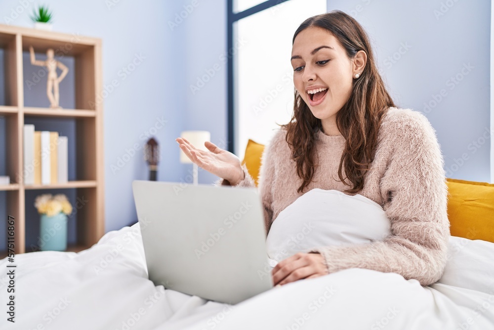 Young hispanic woman using computer laptop on the bed celebrating achievement with happy smile and winner expression with raised hand Young hispanic woman using computer laptop on the bed celebrating achievement with happy smile and winner expression with raised hand