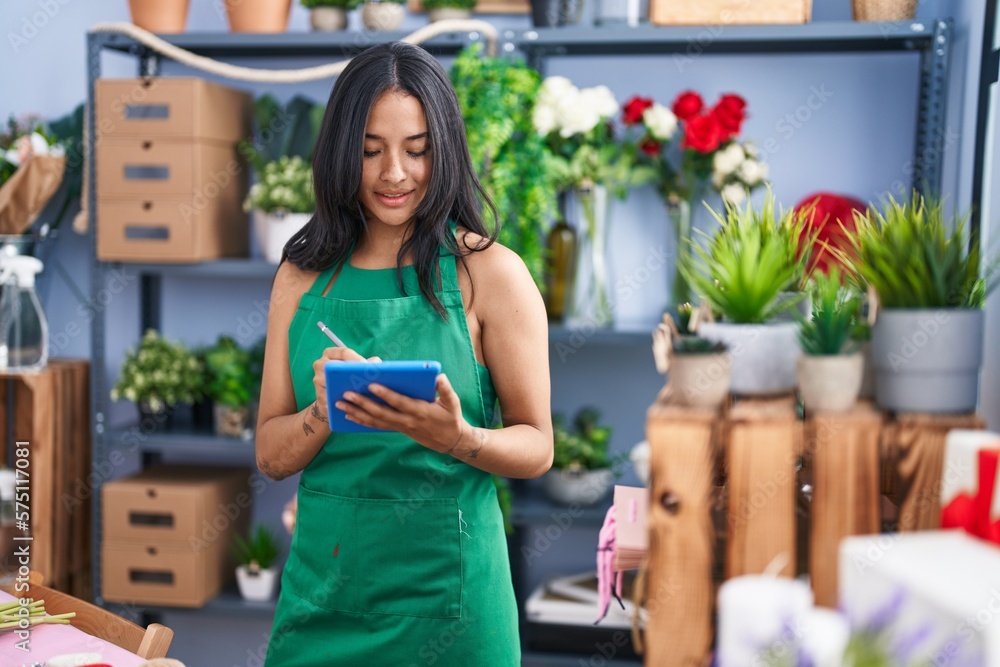 Young hispanic woman florist smiling confident using touchpad at florist shop