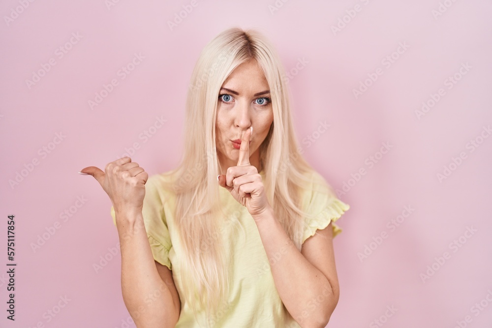 Caucasian woman standing over pink background asking to be quiet with finger on lips pointing with hand to the side. silence and secret concept. Caucasian woman standing over pink background asking to be quiet with finger on lips pointing with hand to the side. silence and secret concept.