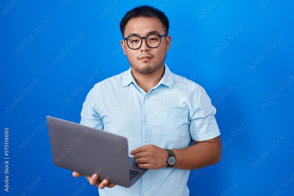 Chinese young man using computer laptop relaxed with serious expression on face. simple and natural looking at the camera. Chinese young man using computer laptop relaxed with serious expression on face. simple and natural looking at the camera.