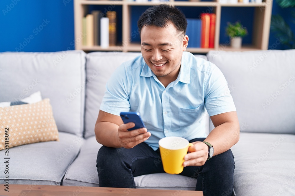 Young chinese man using smartphone drinking coffee at home Young chinese man using smartphone drinking coffee at home