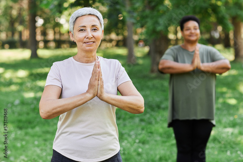 Waist up portrait of smiling senior woman enjoying yoga outdoors and looking at camera while doing breathing exercises, copy space