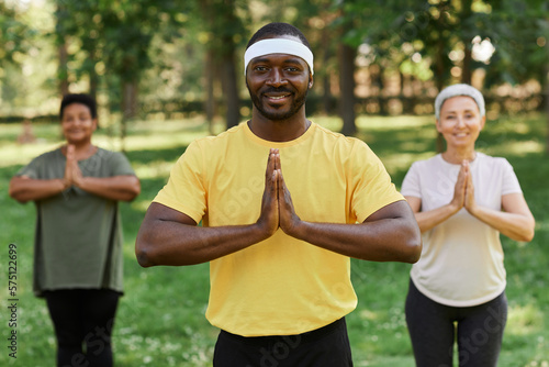 Waist up portrait of male yoga instructor smiling at camera in park with senior women in background