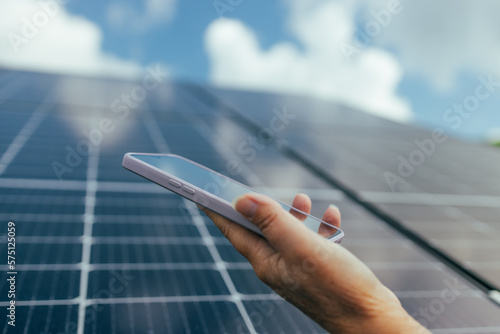Foto Man using smartphone for controlling photovoltaic solar power station producing green eco friendly energy