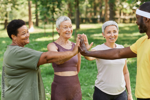 Group of active senior women high five with trainer after enjoying outdoor workout in park
