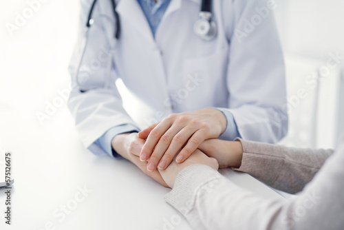Doctor and patient sitting at the table in clinic office. The focus is on female physician's hands reassuring woman, only hands close up. Medicine concept