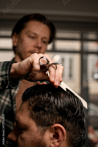 selective focus on hand of barber with hair scissors and comb accurate combing the wet hair of client