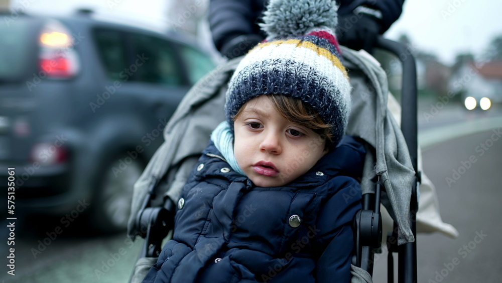 Child strolling in street during winter season. Parent pushing little boy wearing beanie and coat during cold December month Child strolling in street during winter season. Parent pushing little boy wearing beanie and coat during cold December month