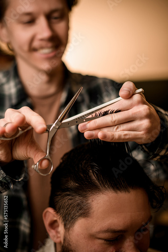 selective focus on scissors in the hands of barber who professionally cuts hair of client in barbershop.