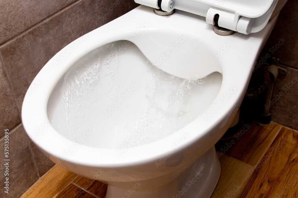 Toilet while flushing urine with water. A stream of water in the toilet