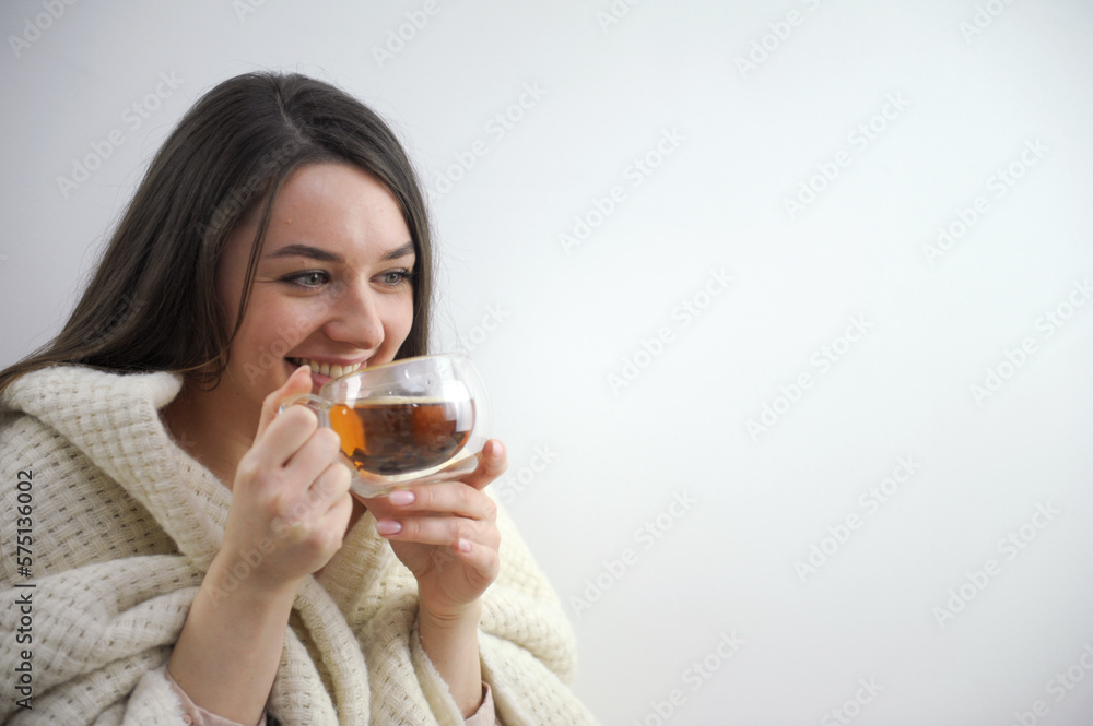 Portrait of sick modern 20 years old housewife in roll neck sweater and cardigan showing cup of hot tea with ginger, lemon and honey isolated on winter light blue background. High quality photo Portrait of sick modern 20 years old housewife in roll neck sweater and cardigan showing cup of hot tea with ginger, lemon and honey isolated on winter light blue background. High quality photo