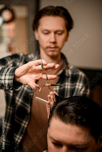 selective focus on scissors in the hands of barber who masterfully cuts hair of client in barbershop.