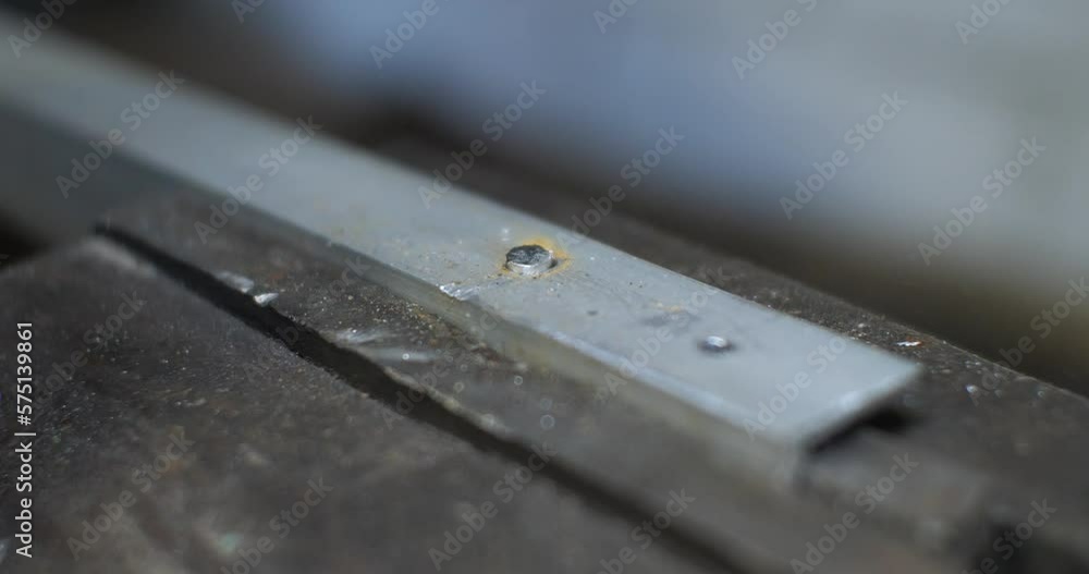 In the of a man, he hammers a metal rivet with a hammer. The