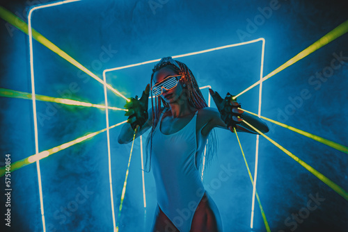 Young woman dancer posing in dark night club interior with blue lights green lasers