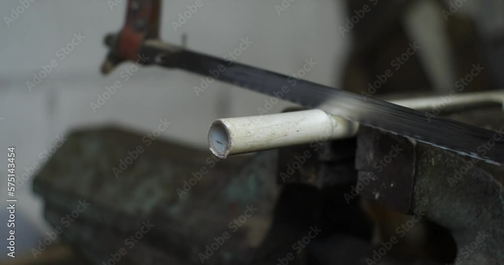 A hand saw for metal saws off a pipe. A man saws off a piece of a water