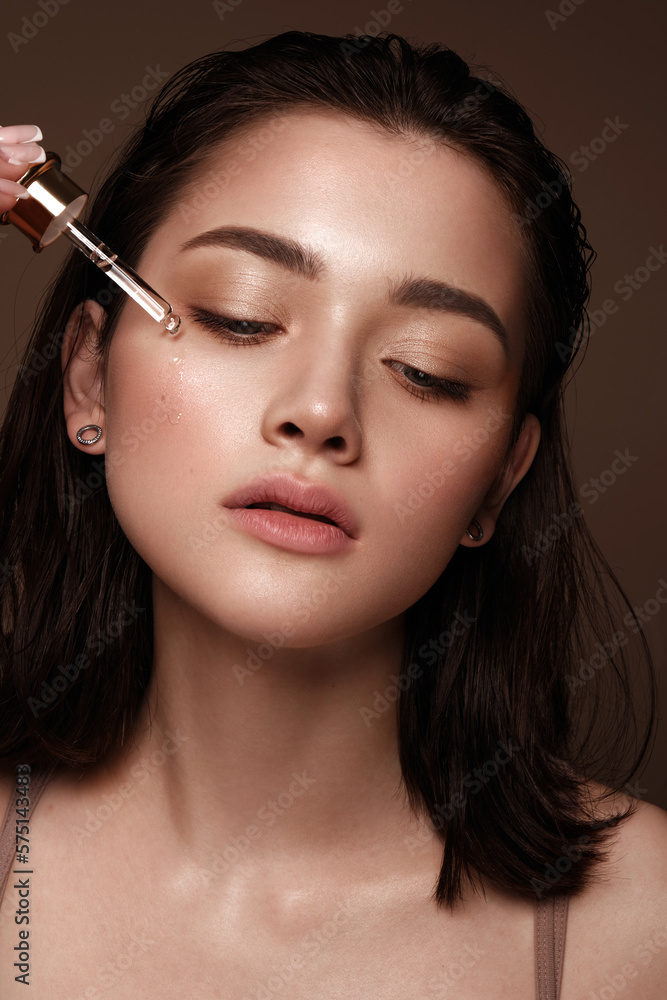 Beautiful young girl with natural nude make-up with cosmetics oil in hands. Beauty face.