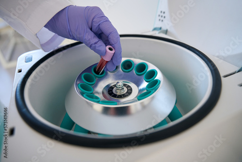 Laboratory assistant puts test tube with blood sample into centrifuge