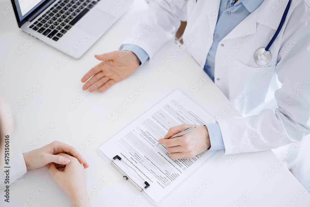 Doctor and patient discussing current health questions while sitting opposite of each other and using clipboard at the table in clinic, just hands closeup. Medicine concept Doctor and patient discussing current health questions while sitting opposite of each other and using clipboard at the table in clinic, just hands closeup. Medicine concept