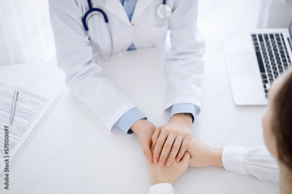 Doctor and patient sitting opposite each other at the table in clinic office. The focus is on female physician's hands reassuring woman, only hands, close up. Medicine concept Doctor and patient sitting opposite each other at the table in clinic office. The focus is on female physician's hands reassuring woman, only hands, close up. Medicine concept