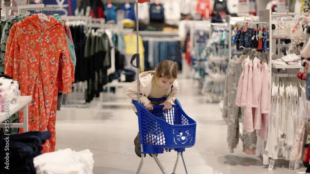 Little girl is having fun in a clothes store, riding a shopping cart Little girl is having fun in a clothes store, riding a shopping cart